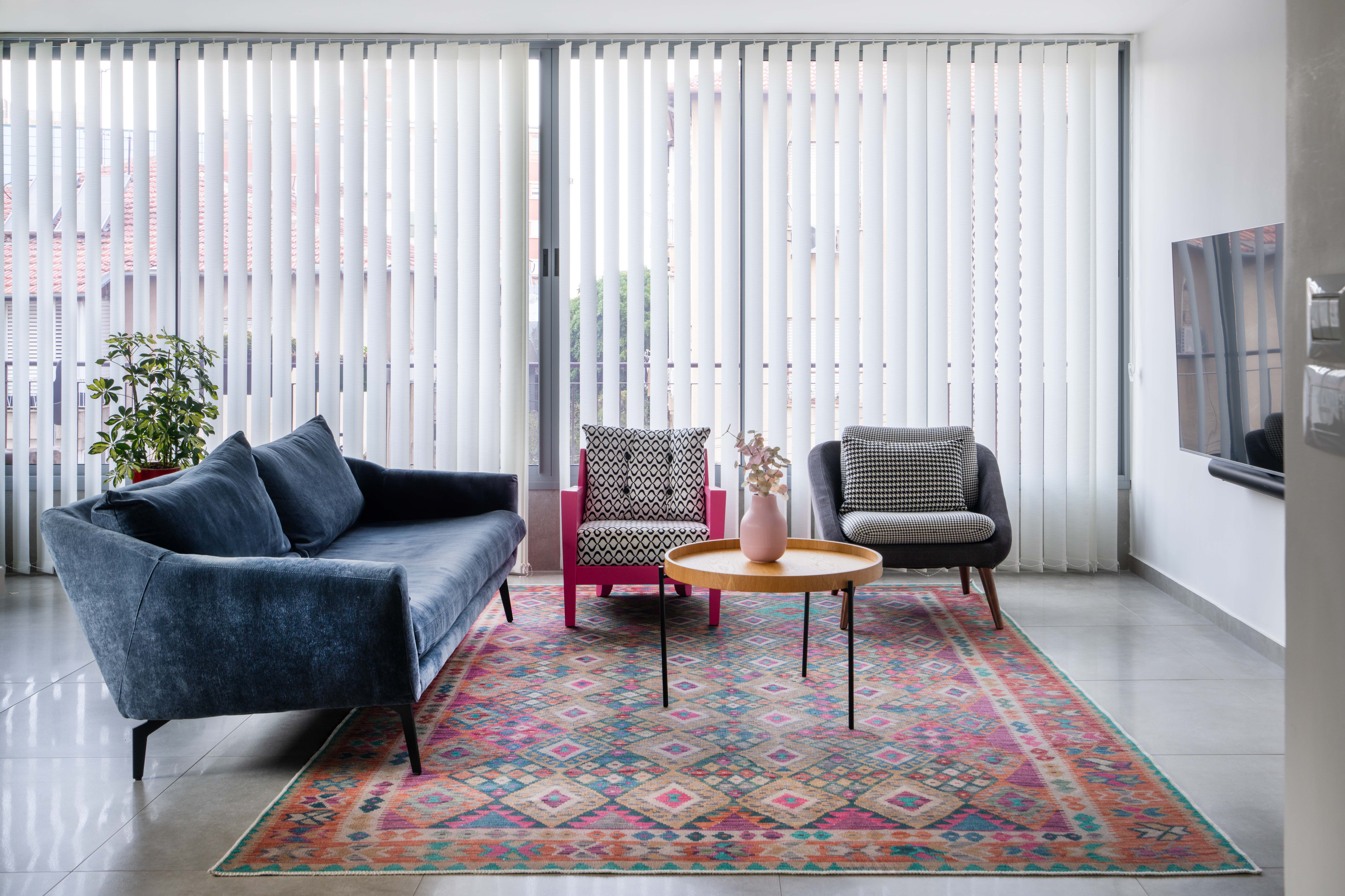 תמונה של סלון צבעוני.ספה כחולה שטיח צבעוני, כורסה ורודה וכורסה אפורה