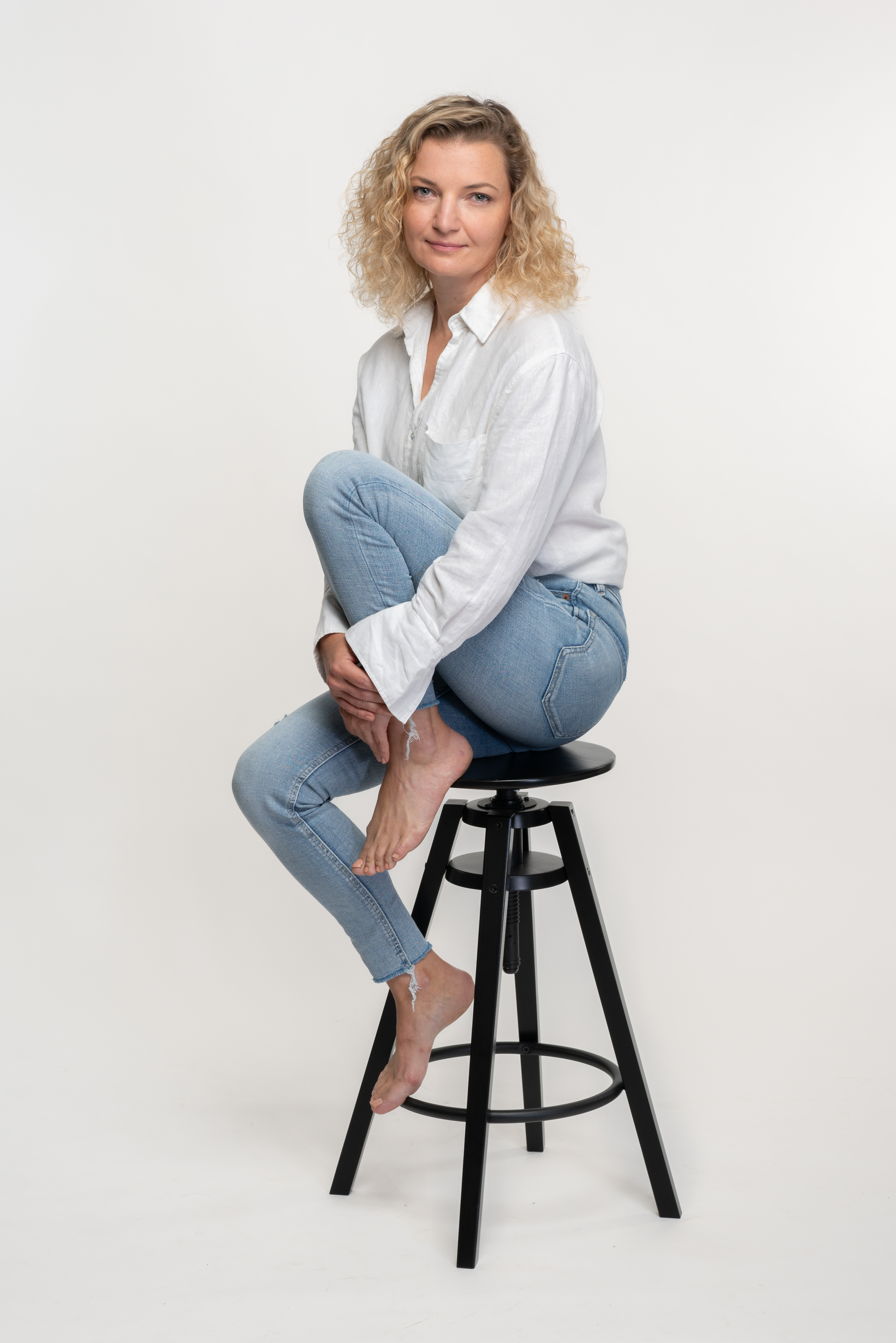 מצולמת עם גינס וחולצה לבנה יושבת על כיסא שחור ורקע לבן