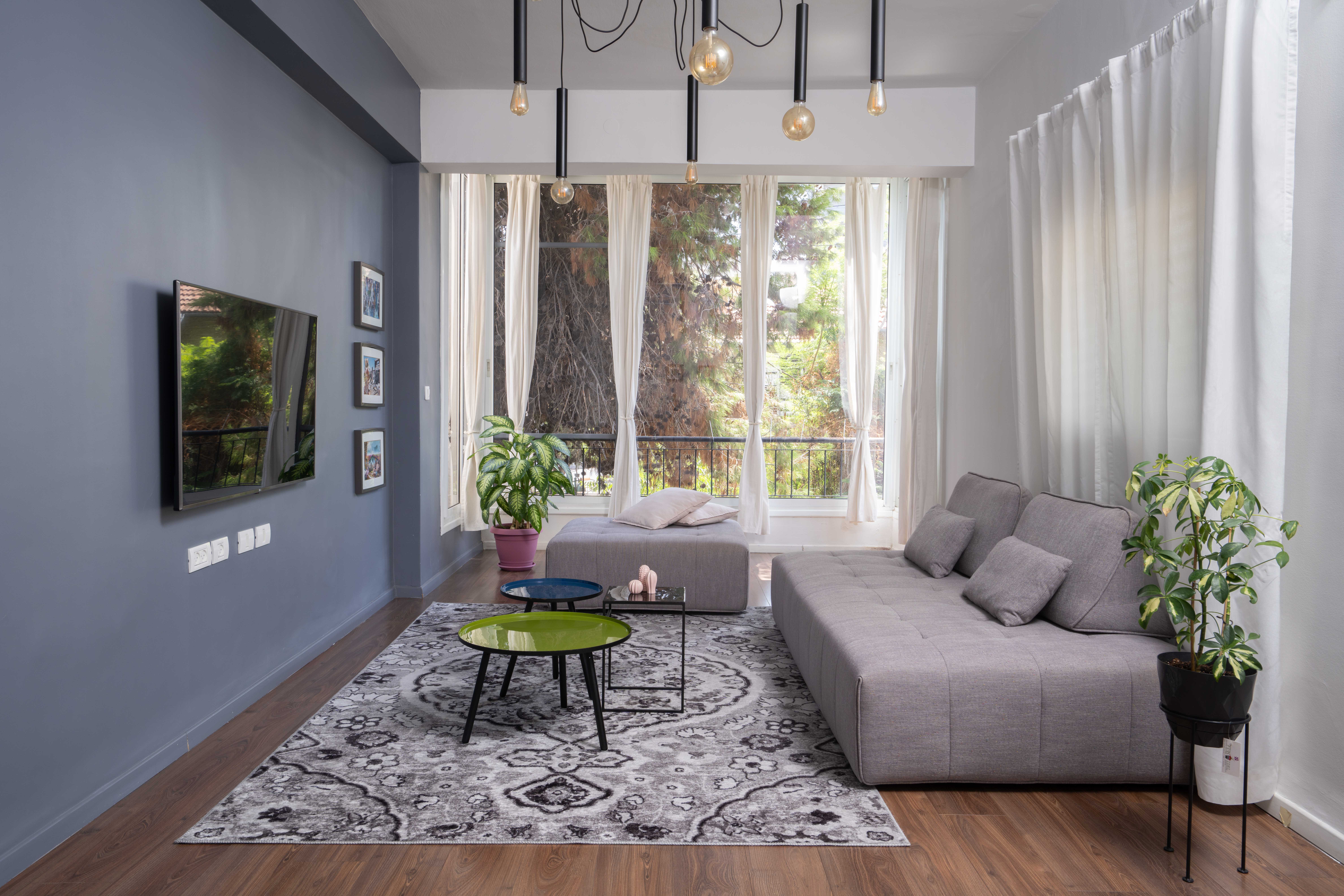 סלון עם קיר אפור ספה אפורה וגופי תאורה שחורים מהתקרה עם כורסת ספת חמור ירוקה שולחנות קפה עגולים צבעוניים