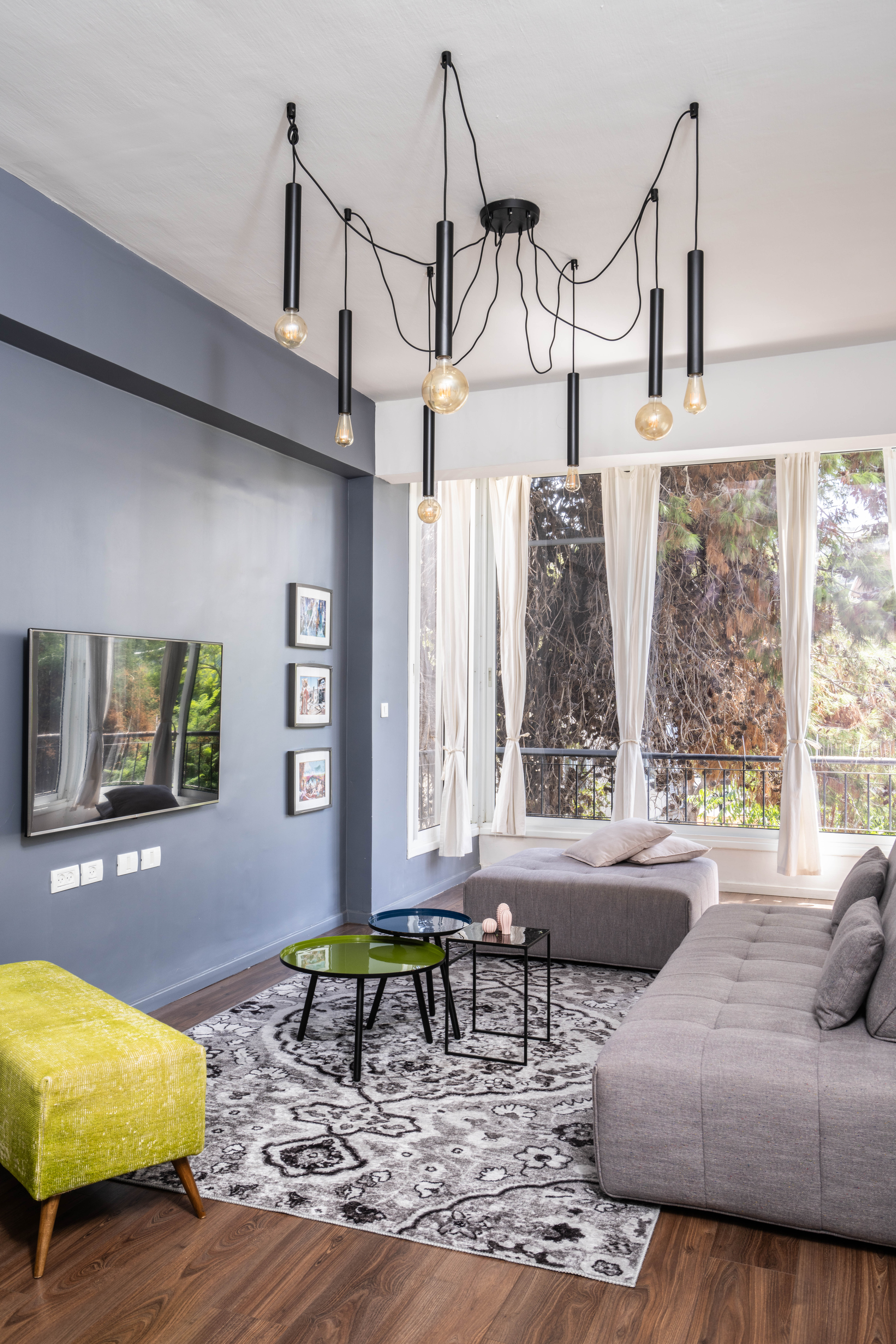 תמונה של סלון עם קיר אפור ספה אפורה שפת חמור ירוקה ושולחנות קפה עגולים צבעוניים