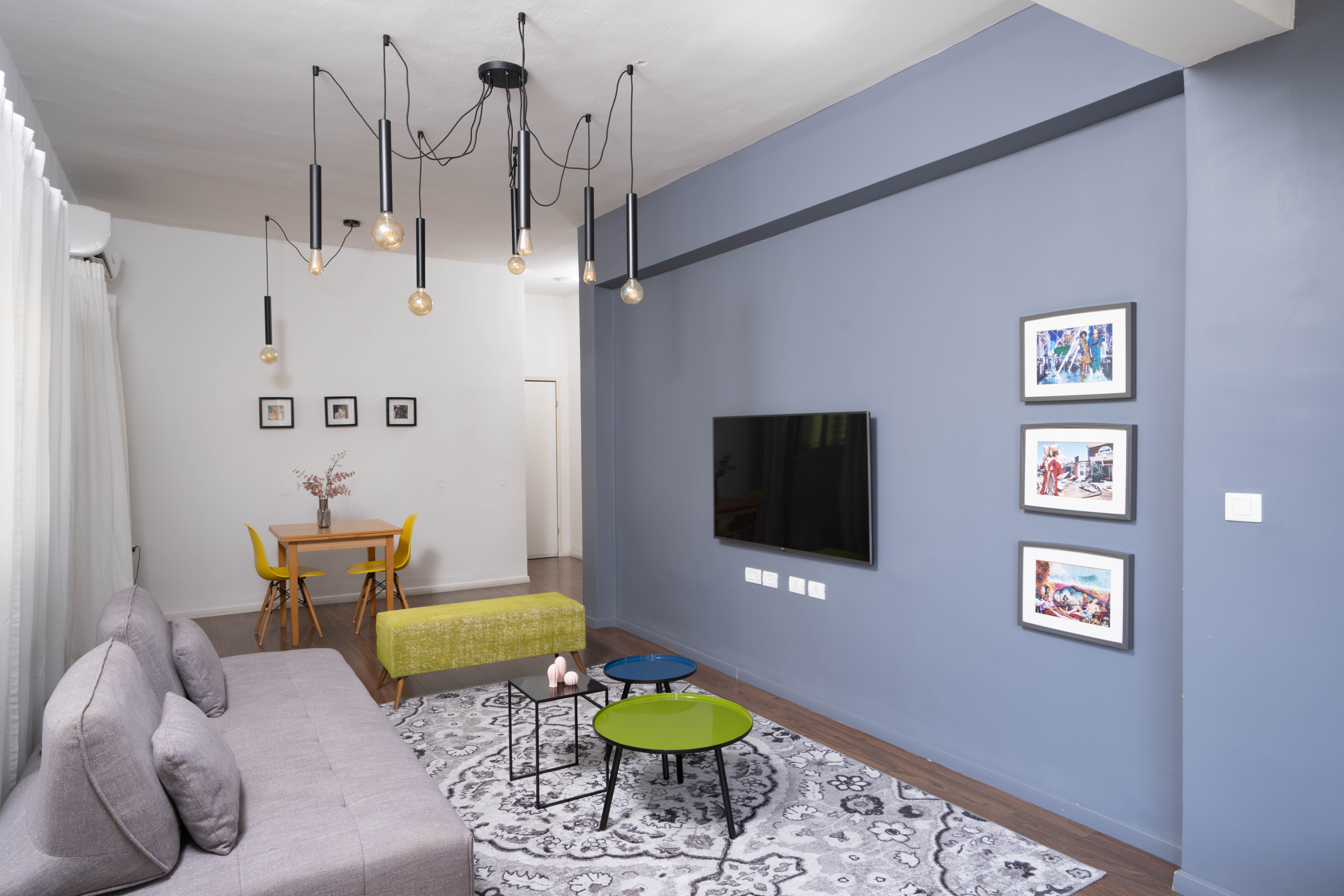 תמונה של סלון עם קיר אפור ספה אפורה שפת חמור ירוקה ושולחנות קפה עגולים צבעוניים