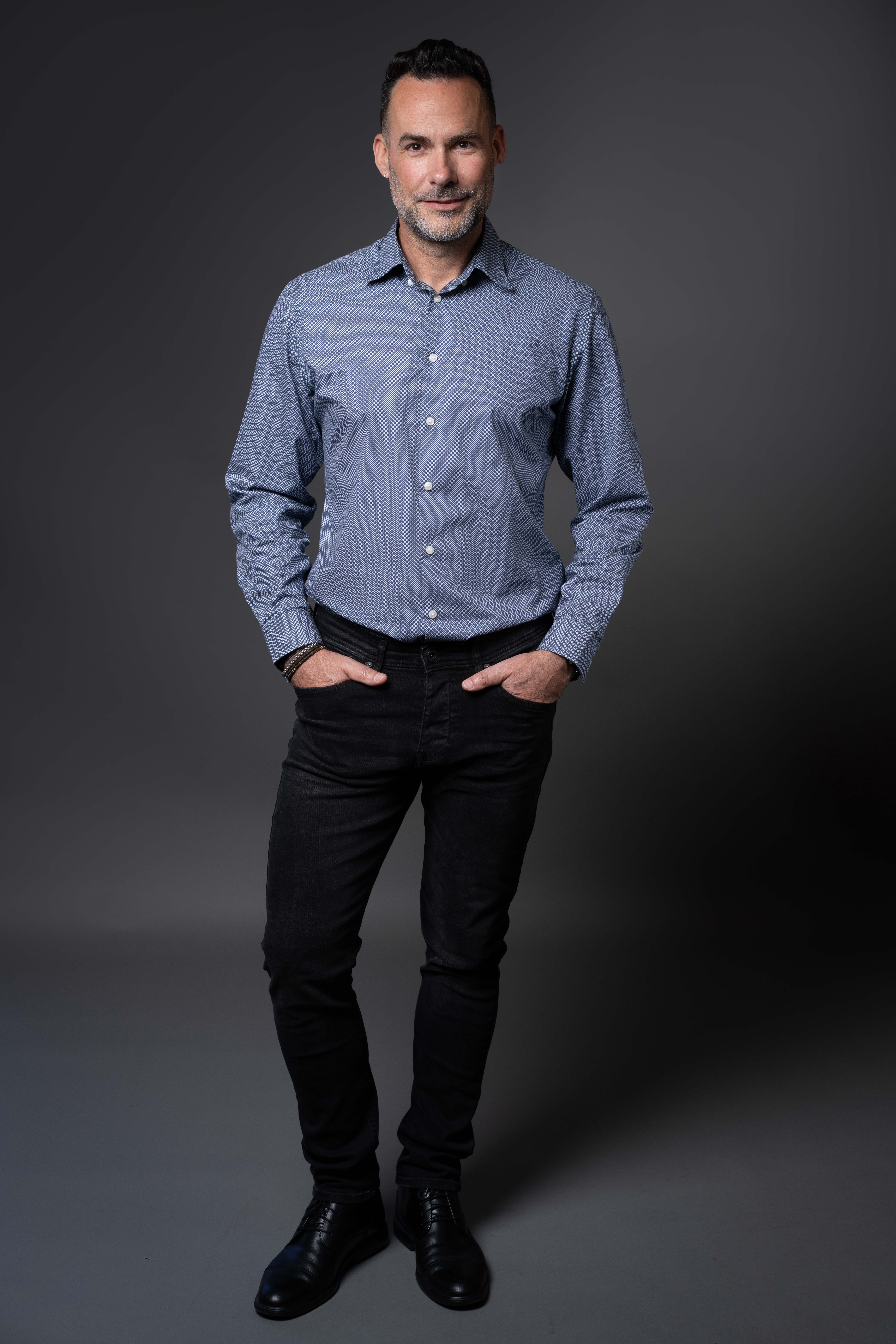 גבר עומד עם ידיים בכיסים על רקע כהה